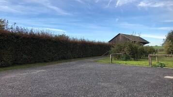 A gravel driveway leading to a wooden barn with a metal gate.