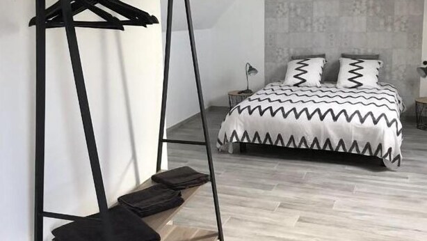 A bedroom with a bed, a hanging light fixture, a wooden shelf, and a black metal hanger stand. - Iris - Bed and breakfast (Ognes)