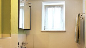 Un baño pequeño con lavamanos, espejo, ventana y una toalla colgada en la pared.