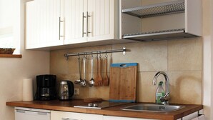 Una cocina compacta con armarios blancos, encimera de madera, lavavajillas integrado y un colgador para utensilios.