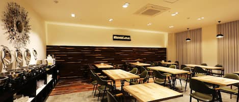 Une salle à manger d’hôtel avec plusieurs tables et chaises, un buffet proposant divers plats et un panneau fixé au mur.