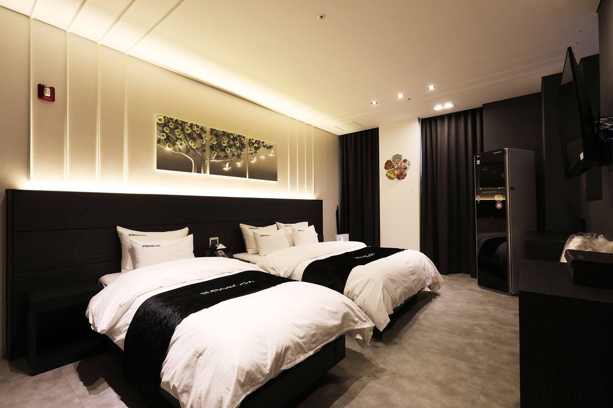 Habitación de hotel moderna con dos camas, una obra de arte grande en la pared, un televisor de pantalla plana y un refrigerador empotrado.