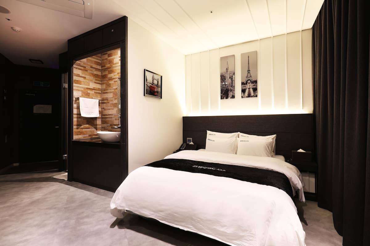 Una habitación de hotel moderna con una cama grande, baño integrado y una obra de arte con vistas a la ciudad.