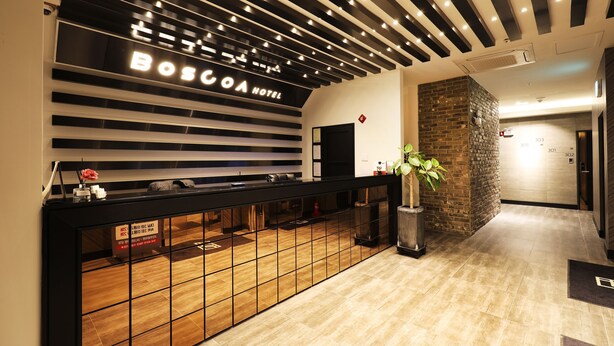 A reception area with a modern design, featuring a black reception desk, a sign for Bosca Hotel, and a brick accent wall. - Wonju Boscoa Hotel (Wonju)