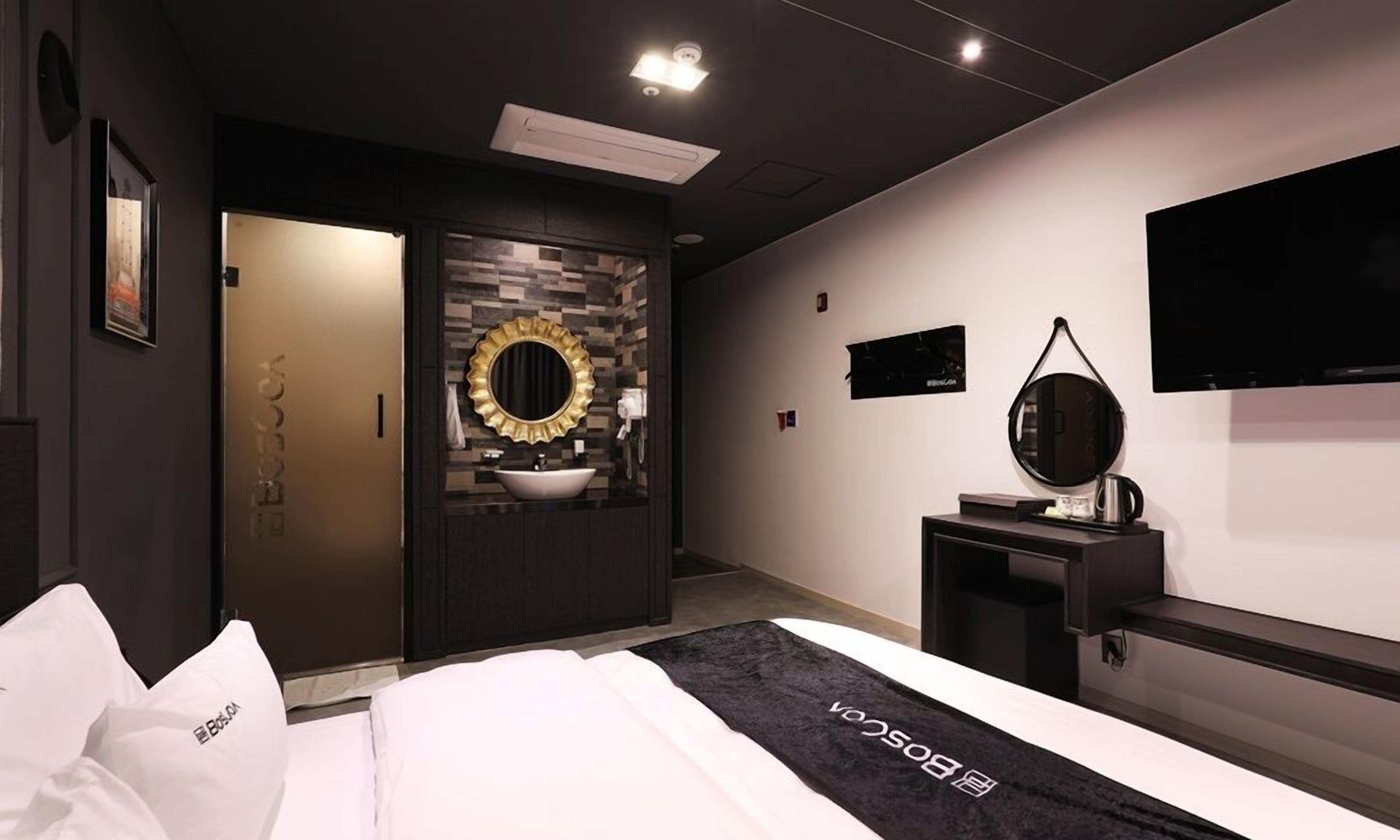 Una habitación de hotel moderna con una cama, un tocador con espejo, una televisión y una puerta que da a otra habitación.