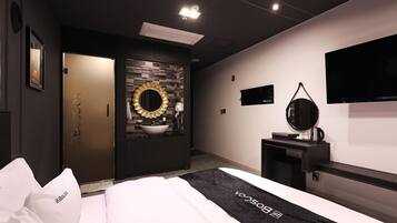 Una habitación de hotel moderna con una cama, un tocador con espejo, una televisión y una puerta que da a otra habitación.