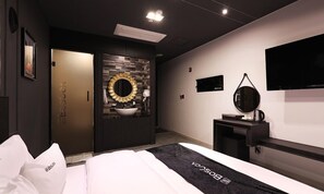 A modern hotel room with a bed, a vanity with a mirror, a television, and a door leading to another room.