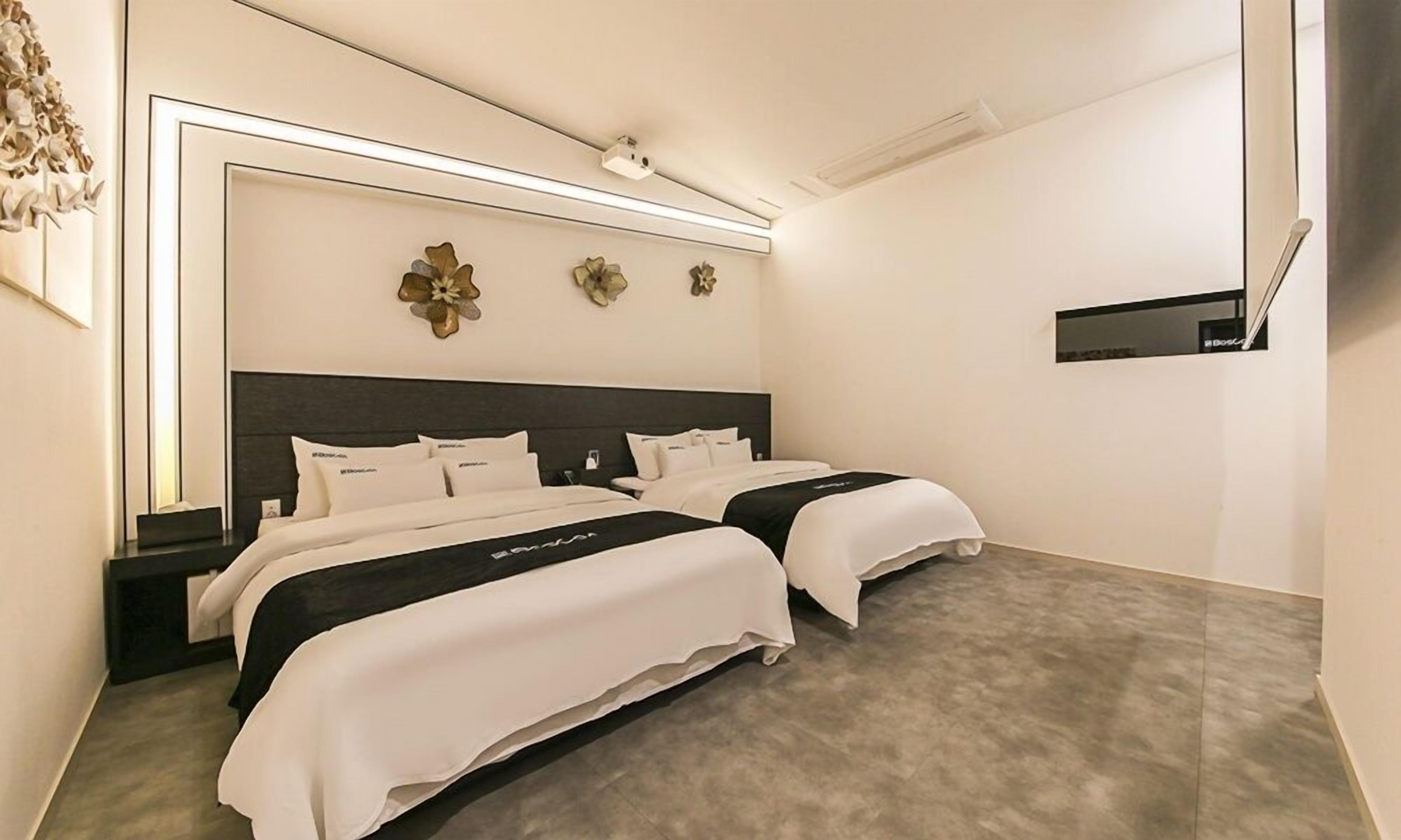 Habitación de hotel con dos camas, cabecera oscura y televisor montado en la pared.
