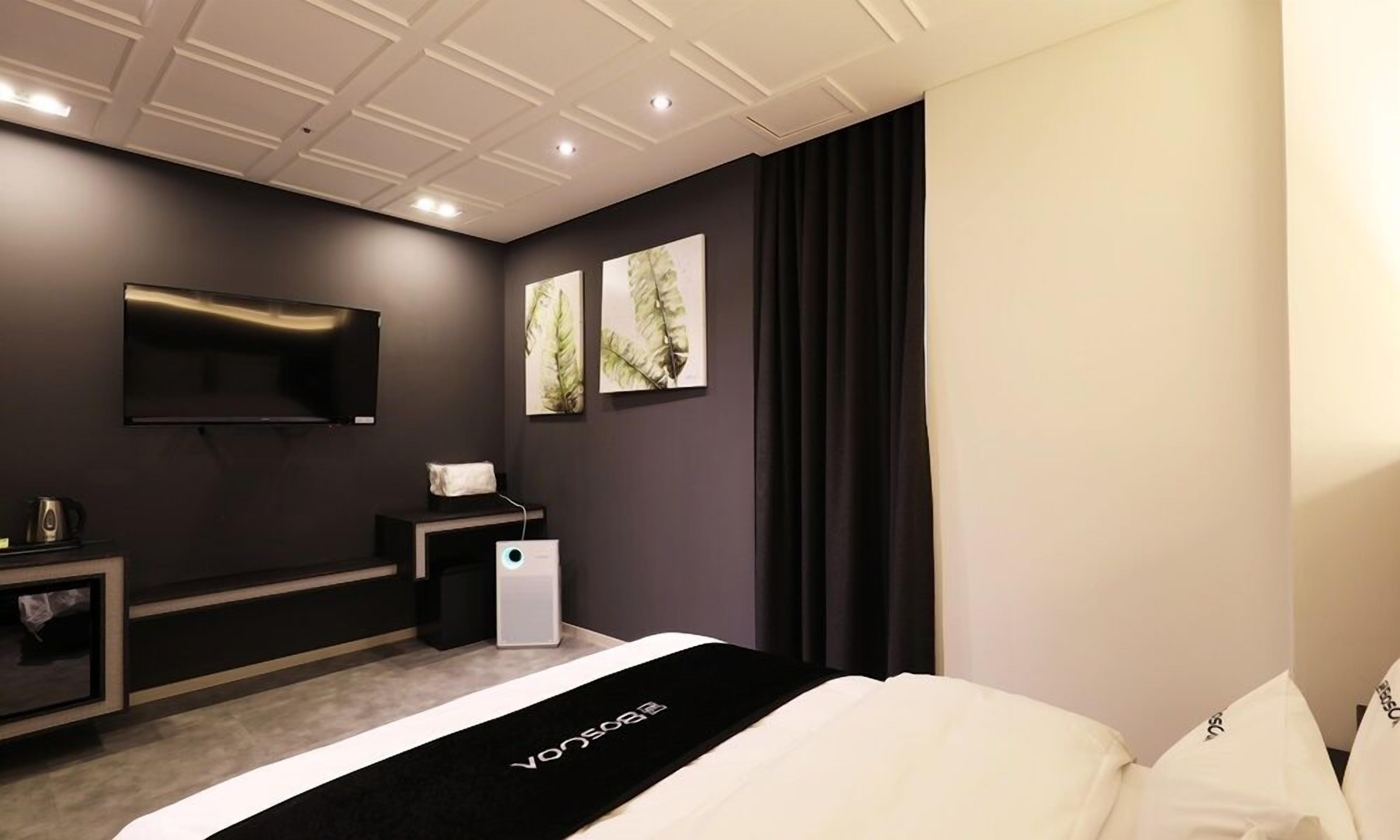 Una habitación de hotel moderna con televisión de pantalla plana, un escritorio, una silla y una cama con colcha blanco y negro.