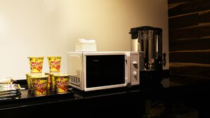A microwave oven with a coffee maker and several containers of instant noodles on a countertop. - Wonju Boscoa Hotel (Wonju)