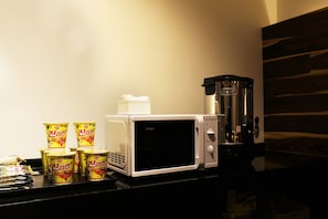 Un microondas con una cafetera y varios envases de fideos instantáneos sobre una encimera.