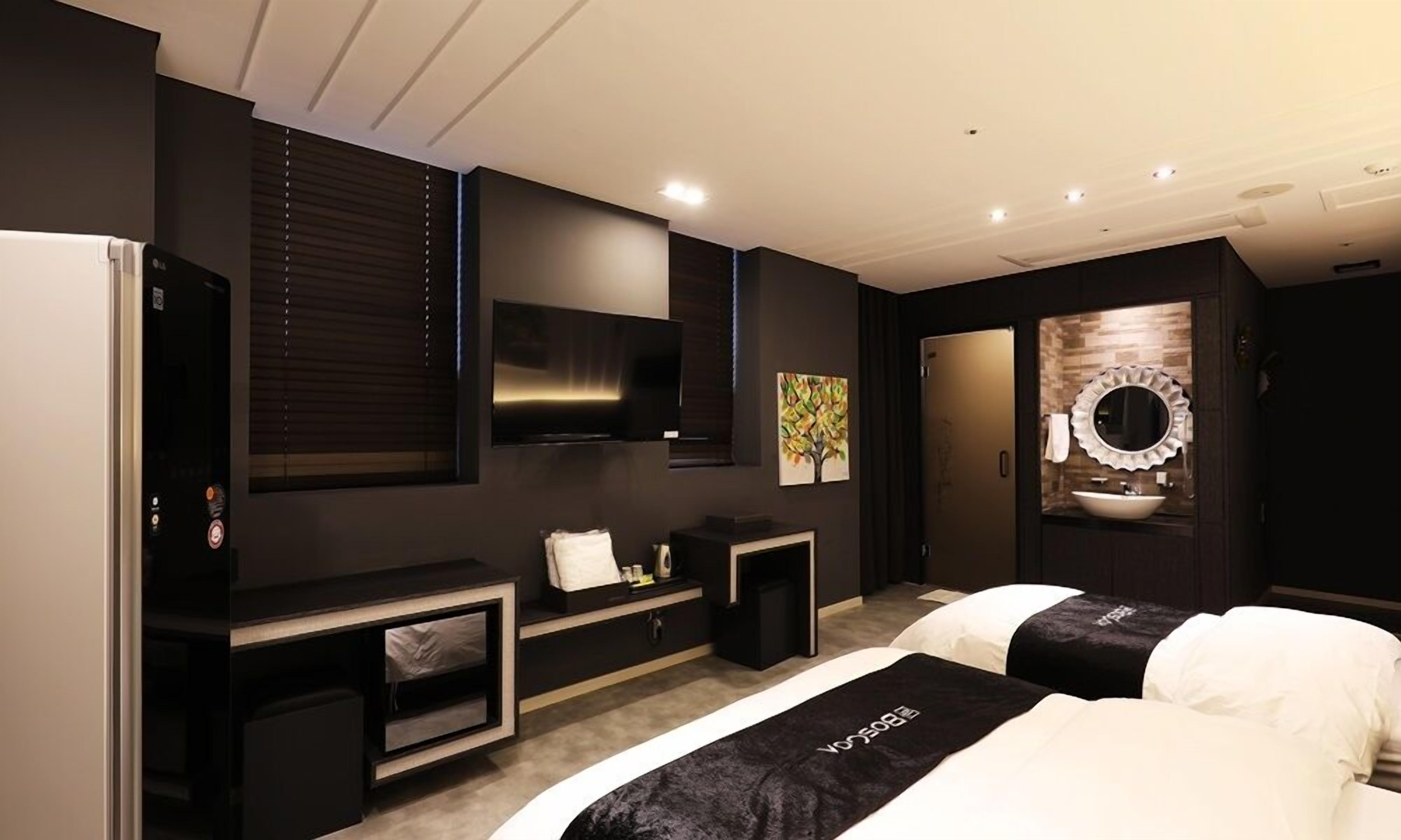 A modern hotel room with a large bed, a TV, a small desk, and a bathroom with a mirror and sink.