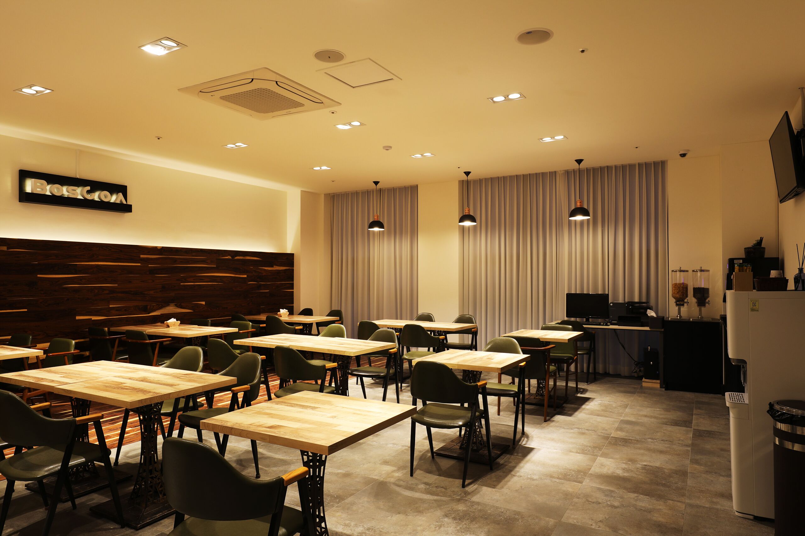 A conference room with multiple tables and chairs, a wooden accent wall, and a large window with curtains.