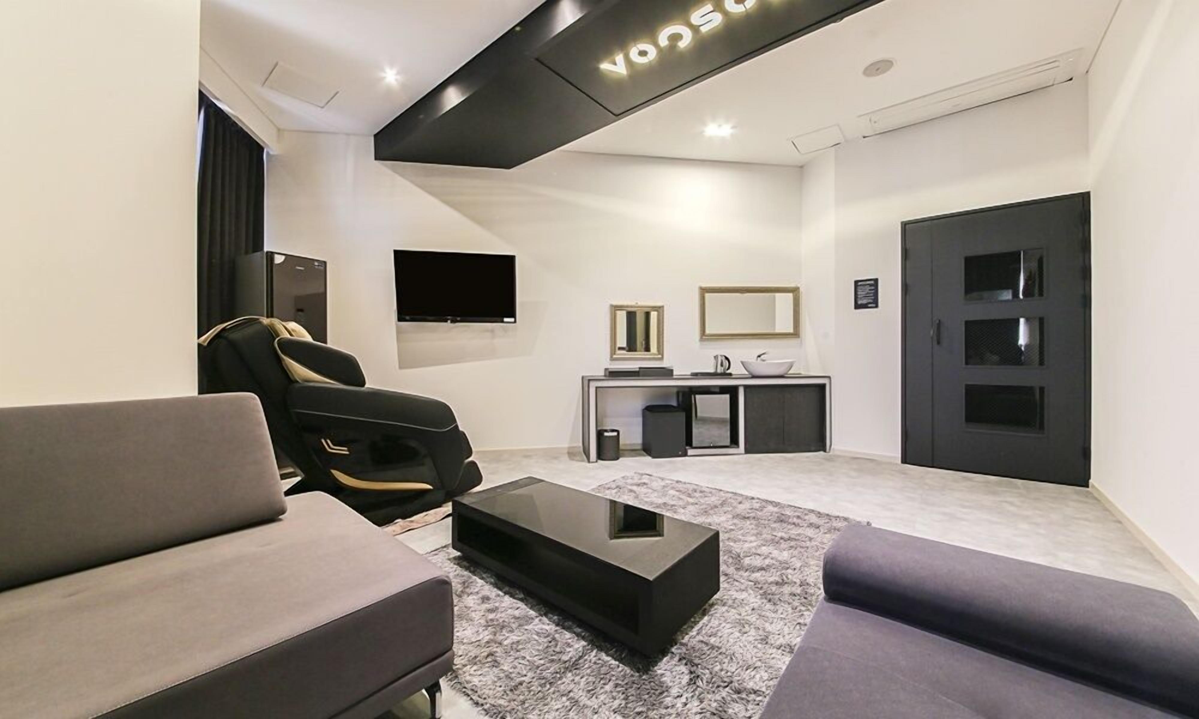 A modern living room with a sofa, a recliner, a coffee table, a flat-screen TV, a mirror, and a door.