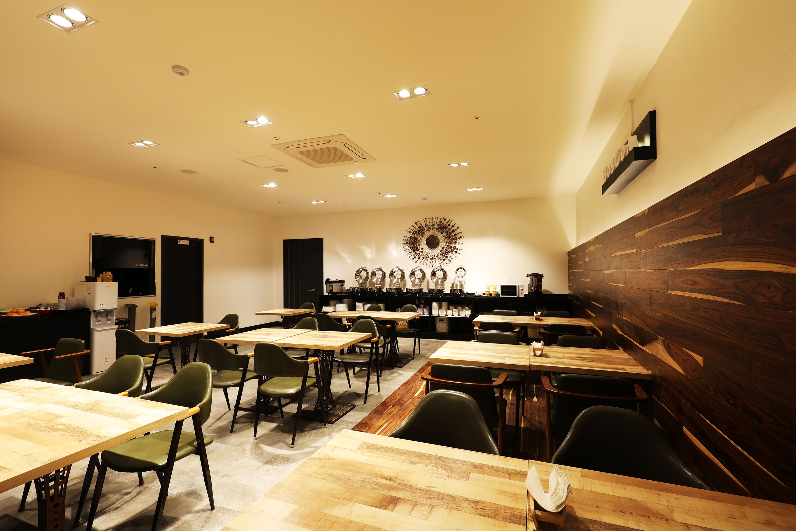 Une salle de conférence dotée de plusieurs tables et chaises, d’un mur d’accent en bois et d’un luminaire décoratif au plafond.