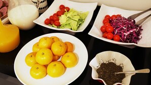 A table with various food items including oranges, lettuce, cherry tomatoes, and shredded cabbage. - Wonju Boscoa Hotel (Wonju)