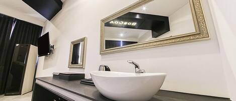 Un baño moderno con lavamanos blanco, dos espejos y un mueble de tocador negro.