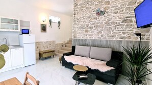 A modern kitchen with white cabinets and a built-in microwave, a cozy living area with a black sofa and a stone accent wall, and a dining area with a wooden table and chairs.