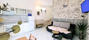 Une cuisine moderne avec des armoires blanches et un micro-ondes encastré, un salon confortable avec un canapé noir et un mur décoratif en pierre, et un coin repas avec une table et des chaises en bois.