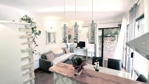 A modern living room with a wooden coffee table, a sofa, and a TV. There are hanging lights and a plant on the wall.