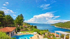 A pool area with lounge chairs, a clear view of the sea, and a mountainous landscape in the background.