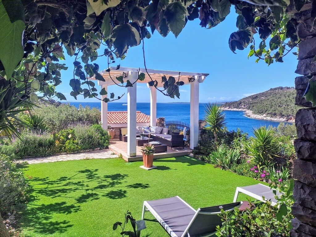 Un patio jardín con pérgola, mobiliario exterior y vista al mar.