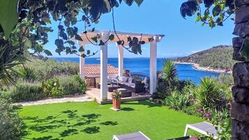 Un patio jardín con pérgola, mobiliario exterior y vista al mar.