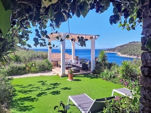 A garden patio with a pergola, outdoor seating, and a view of the sea.