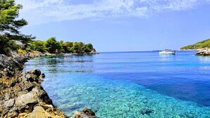 A clear coastal water body with rocky shores and a sailboat in the distance.