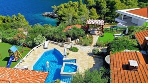 A pool area with a children's play structure, a covered seating area, and a view of the sea.