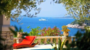 A balcony with a red lounge chair, a view of the sea, and a ship named 'HADROLINJA' in the distance.