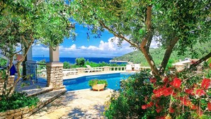 A pool area with stone steps leading to the water, surrounded by lush greenery and a view of the sea.