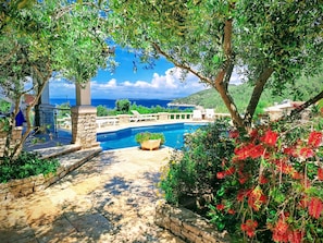 Zona de piscina con escalones de piedra que bajan al agua, rodeada de abundante vegetación y vistas al mar.