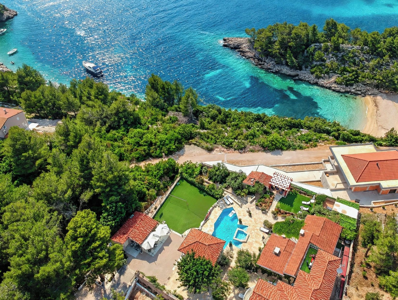 A coastal property with a swimming pool, a tennis court, and a beach.