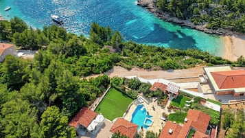 A coastal property with a swimming pool, a tennis court, and a beach.