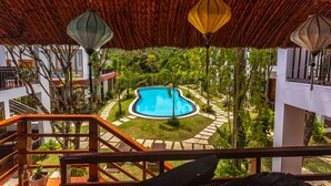 A pool surrounded by greenery, a thatched roof, and a staircase leading to a balcony. - Caesar Phu Quoc Hotel (Phu Quoc)