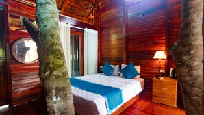 A wooden cabin room with a bed, a nightstand, and a window with a view of the outdoors. - Caesar Phu Quoc Hotel (Phu Quoc)