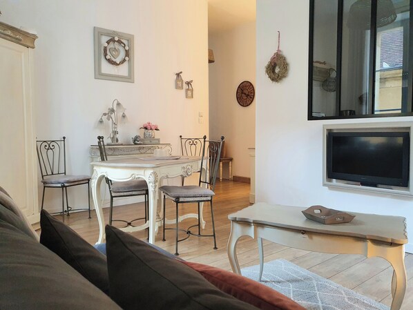 A living room with a sofa, a dining table with chairs, a TV mounted on the wall, and a fireplace.