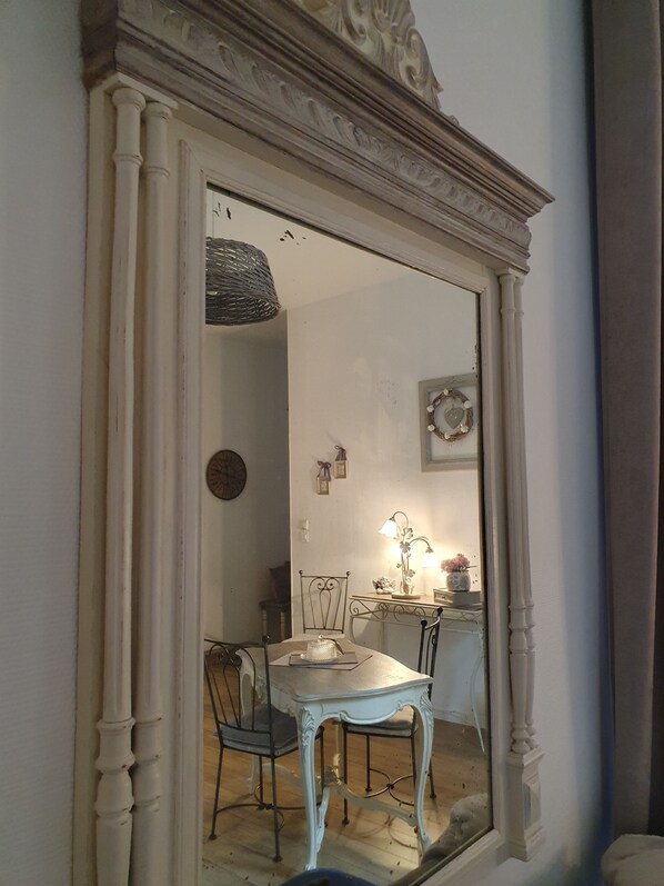 Une pièce avec un grand miroir, une table à manger, des chaises et une petite table avec une lampe.