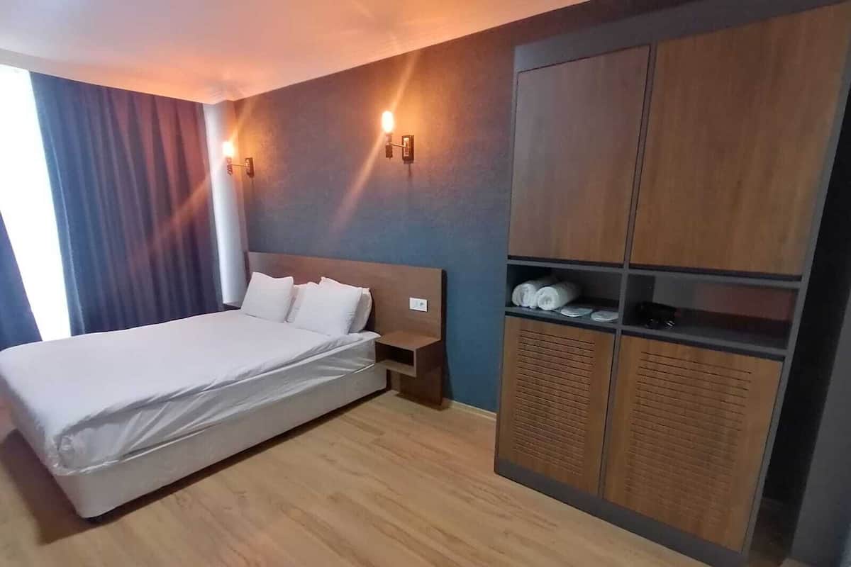 Habitación de hotel con cama, armario de madera y dos luces fijadas a la pared.