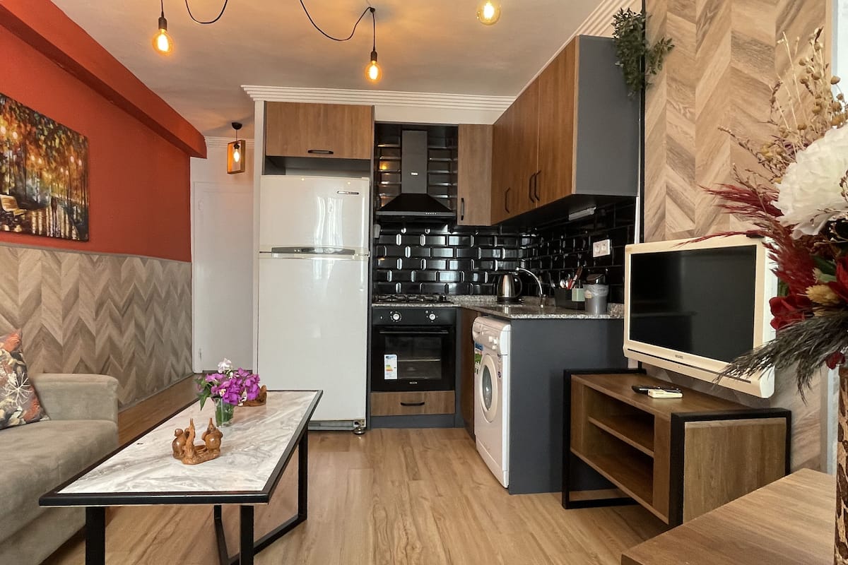 Una cocina compacta con electrodomésticos modernos, un comedor con mesa de mármol y una sala de estar con sofá y elementos decorativos.