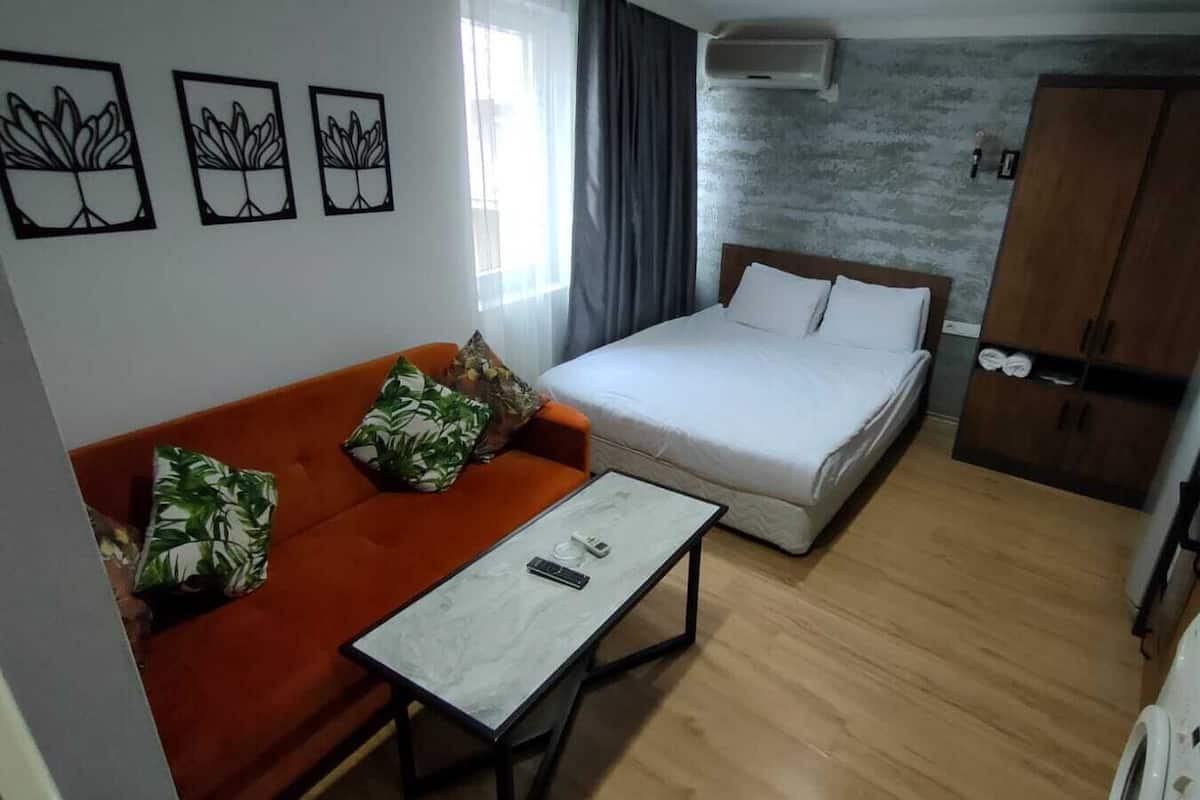 Una habitación compacta con cama, sofá, una mesita y kitchenette.