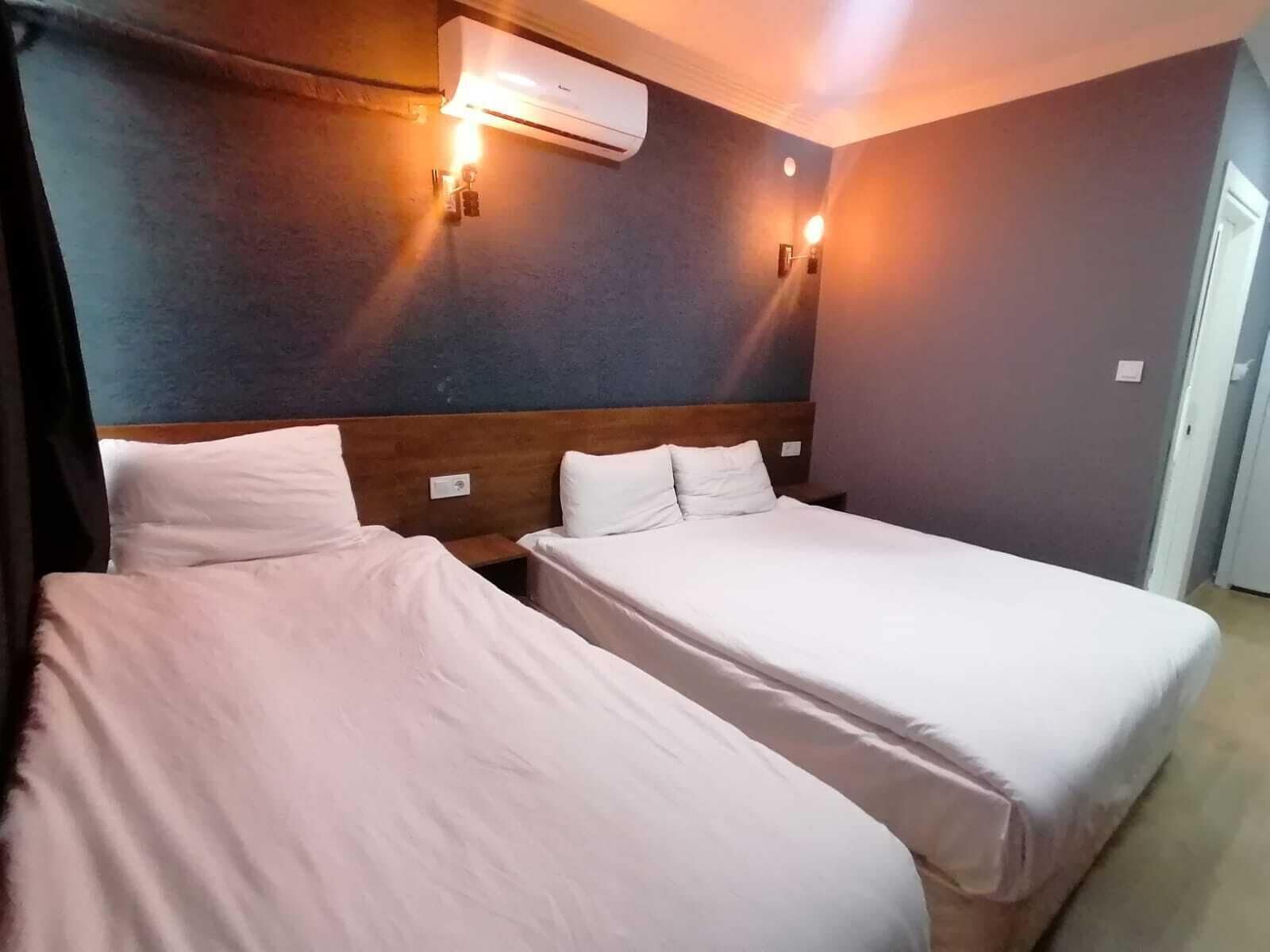 A hotel room with two beds, an air conditioner, and wall-mounted lights.