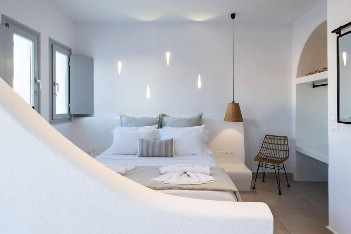 A modern bedroom with a bed, bedside table, chair, and a hanging light fixture.