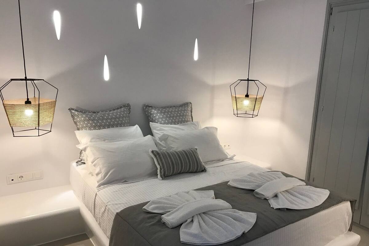 A modern bedroom with a bed, patterned pillows, and two hanging light fixtures.