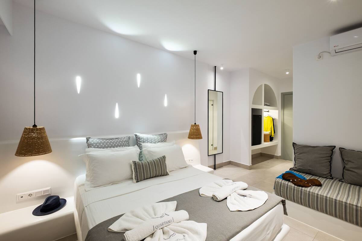 A modern hotel room with a neatly made bed, a sofa, and a hanging light fixture.