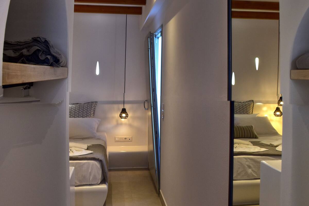 A modern bedroom with a built-in wardrobe, a small seating area, and a large mirror.