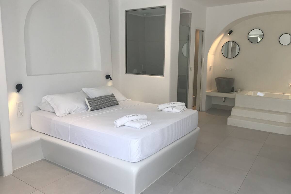 A modern bedroom with a large bed, a walk-in shower, and a bathroom with a bathtub and sink.