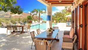 Un patio exterior con piscina, zona de comedor y sillones de descanso.