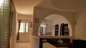 A living room with a sofa, a coffee table, and a bookshelf. There is a door with a window and a curtain. - 'DAR Leyla' CHARMING VILLA WITH POOL.... AT THE HEART OF THE DJERBIAN CAMPAIGN (Mezraya)